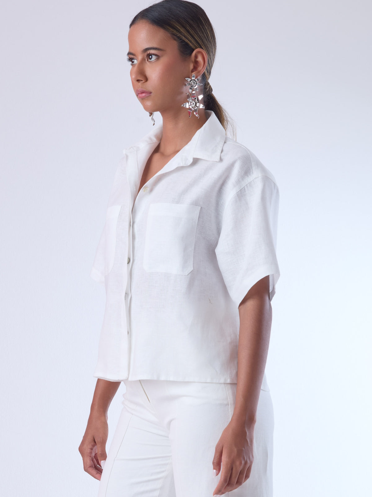 Blusa de corte recto y estilo relajado con manga corta amplia y cuello clásico. Está confeccionada en un tejido ligero y fresco, ideal para climas cálidos. Tiene dos bolsillos frontales de parche a la altura del pecho y una tapeta central que oculta los botones, lo que aporta un acabado limpio y pulido. Su diseño versátil combina elegancia casual y comodidad.