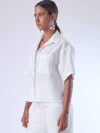 Blusa de corte recto y estilo relajado con manga corta amplia y cuello clásico. Está confeccionada en un tejido ligero y fresco, ideal para climas cálidos. Tiene dos bolsillos frontales de parche a la altura del pecho y una tapeta central que oculta los botones, lo que aporta un acabado limpio y pulido. Su diseño versátil combina elegancia casual y comodidad.