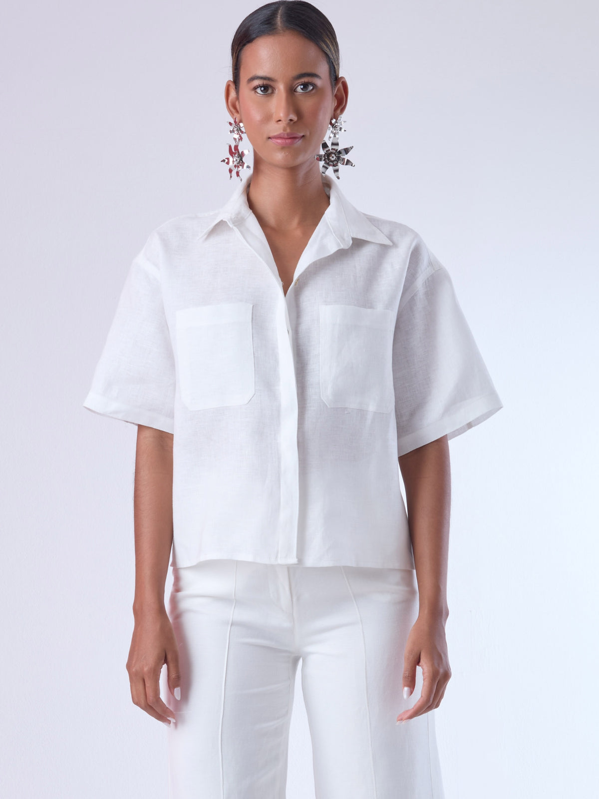 Blusa de corte recto y estilo relajado con manga corta amplia y cuello clásico. Está confeccionada en un tejido ligero y fresco, ideal para climas cálidos. Tiene dos bolsillos frontales de parche a la altura del pecho y una tapeta central que oculta los botones, lo que aporta un acabado limpio y pulido. Su diseño versátil combina elegancia casual y comodidad.