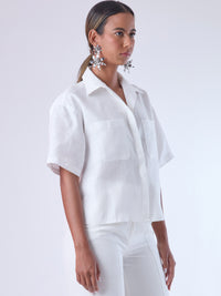 Blusa de corte recto y estilo relajado con manga corta amplia y cuello clásico. Está confeccionada en un tejido ligero y fresco, ideal para climas cálidos. Tiene dos bolsillos frontales de parche a la altura del pecho y una tapeta central que oculta los botones, lo que aporta un acabado limpio y pulido. Su diseño versátil combina elegancia casual y comodidad.