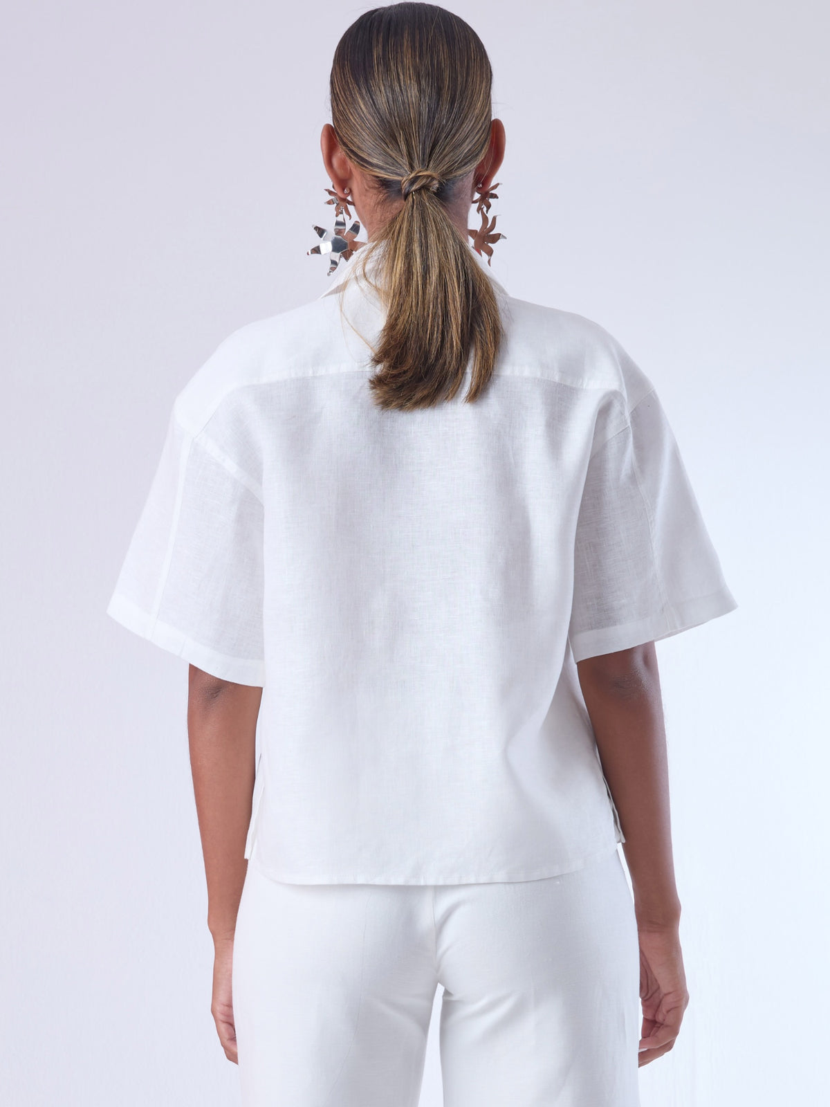 Blusa de corte recto y estilo relajado con manga corta amplia y cuello clásico. Está confeccionada en un tejido ligero y fresco, ideal para climas cálidos. Tiene dos bolsillos frontales de parche a la altura del pecho y una tapeta central que oculta los botones, lo que aporta un acabado limpio y pulido. Su diseño versátil combina elegancia casual y comodidad.