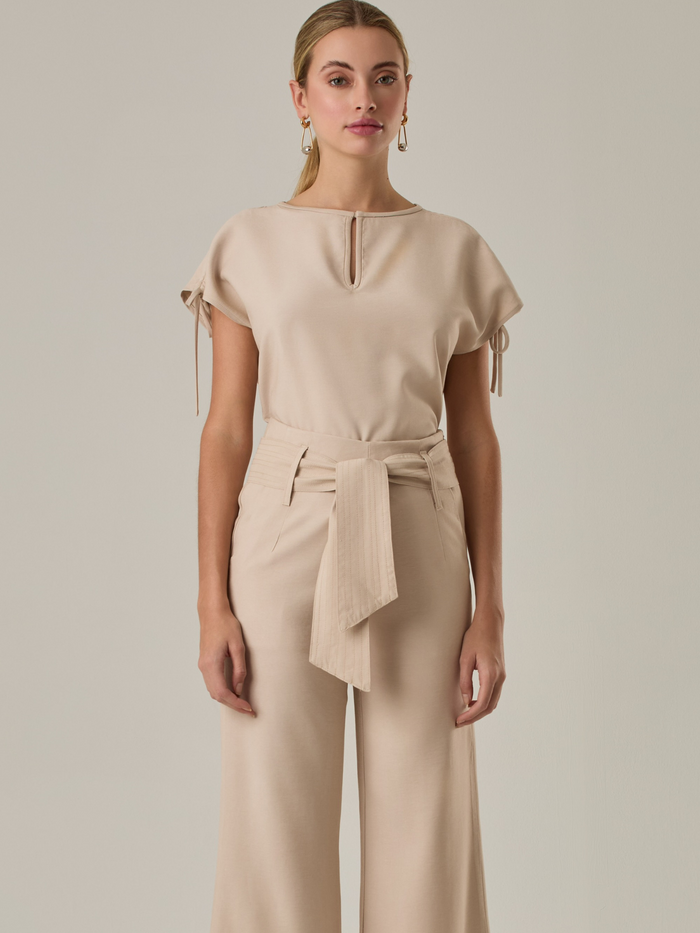 Blusa con  diseño elegante y minimalista. Presenta un sutil escote en forma de lágrima en la parte frontal, mangas cortas con lazos ajustables en los laterales que le aportan un toque delicado y femenino. Su tejido ligero y de textura suave le otorga comodidad y sofisticación.