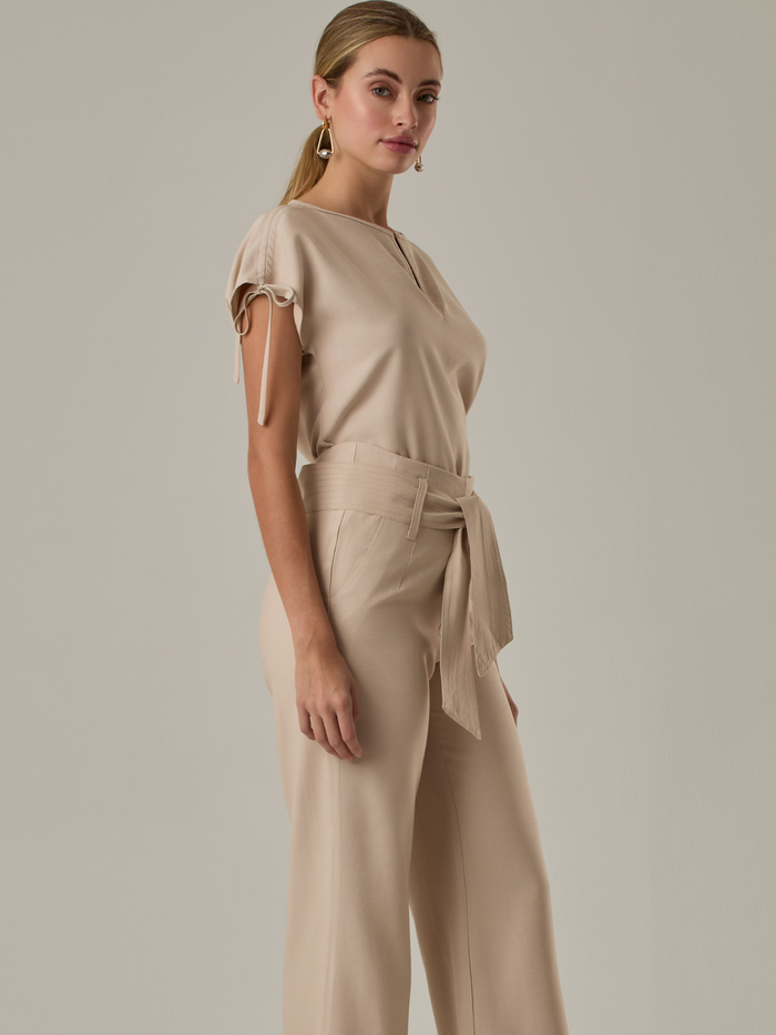 Blusa con  diseño elegante y minimalista. Presenta un sutil escote en forma de lágrima en la parte frontal, mangas cortas con lazos ajustables en los laterales que le aportan un toque delicado y femenino. Su tejido ligero y de textura suave le otorga comodidad y sofisticación.