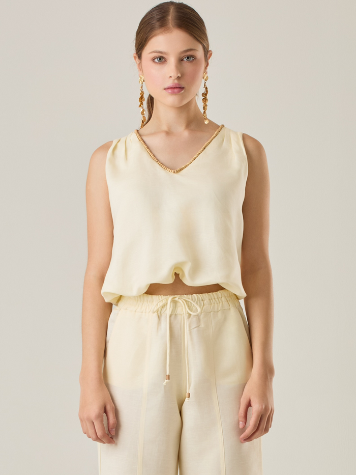 Blusa sin mangas que combina sencillez y sofisticación. El escote en V está realzado por un delicado detalle decorativo que aporta un toque de elegancia. Su corte relajado favorece la comodidad, convirtiéndola en una opción versátil para diferentes ocasiones.