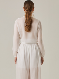 Blusa de manga larga confeccionada en un tejido ligero de textura sutil. Presenta un escote en "V" adornado con un amarre de tiras cruzadas, que añade un toque delicado al diseño. El frente está decorado con volantes que caen en capas suaves, aportando movimiento y un aire romántico. Las mangas tienen un ligero fruncido en los puños, creando un acabado abullonado discreto.

Detalles:

Color: Blanco Perla

Cuidado: Lavar a mano con jabón suave, por separado. No dejar en remojo. Planchar a temperatura alta.


