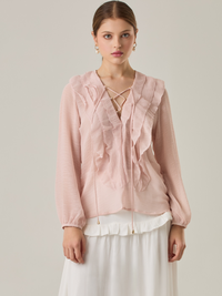 Blusa de manga larga confeccionada en un tejido ligero de textura sutil. Presenta un escote en "V" adornado con un amarre de tiras cruzadas, que añade un toque delicado al diseño. El frente está decorado con volantes que caen en capas suaves, aportando movimiento y un aire romántico. Las mangas tienen un ligero fruncido en los puños, creando un acabado abullonado discreto.

Detalles:

Color: Rosa