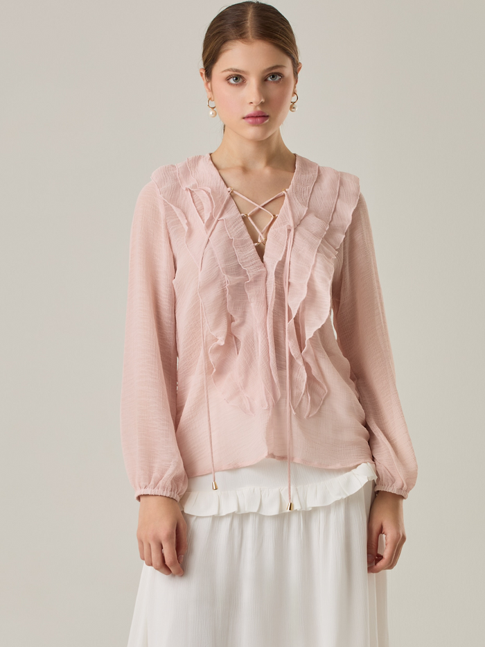 Blusa de manga larga confeccionada en un tejido ligero de textura sutil. Presenta un escote en "V" adornado con un amarre de tiras cruzadas, que añade un toque delicado al diseño. El frente está decorado con volantes que caen en capas suaves, aportando movimiento y un aire romántico. Las mangas tienen un ligero fruncido en los puños, creando un acabado abullonado discreto.

Detalles:

Color: Rosa