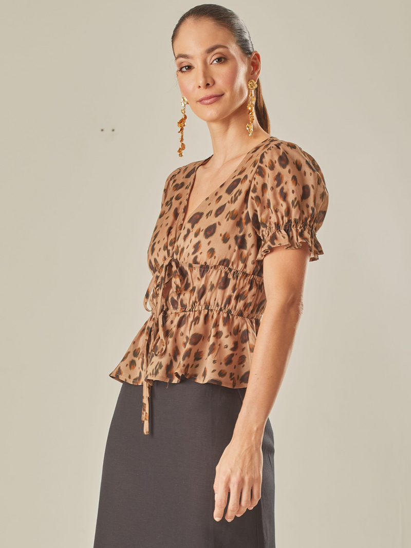 Blusa de mangas cortas, con un escote en V, que incluye una cinta para formar un lazo. Está diseñada con elástico en la cintura y en  las mangas, añadiendo así un detalle sutil que aporta un toque encantador y elegante. 
