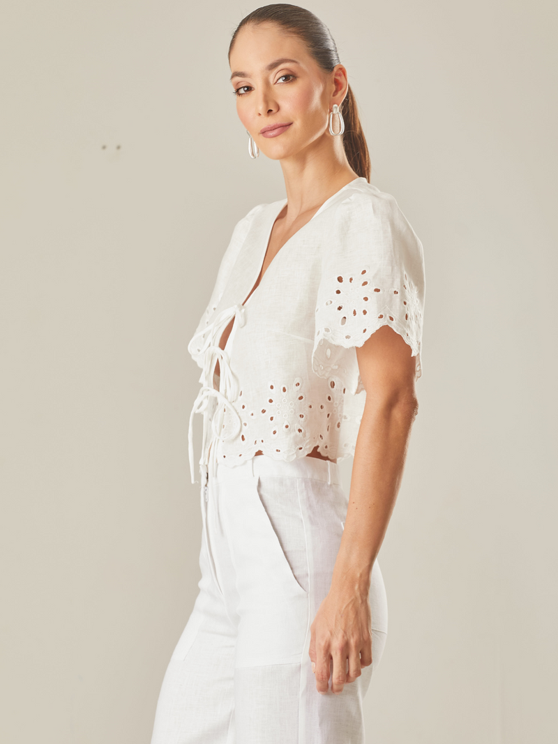 Blusa con guipiur, silueta corta y cierre con finos tirantes delantero, manga corta, estote pico, perfecta para días de playa o eventos especiales por su confección en lino 

Color: Blanco Perla 

Composición: 100% Lino 