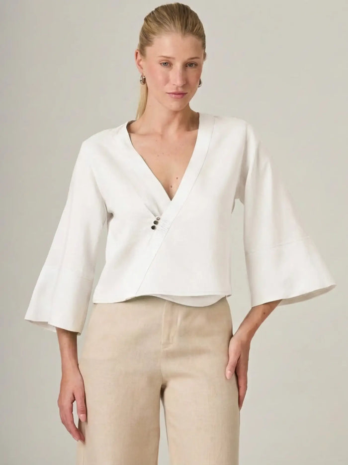 Blusa blanca para mujer con diseño cruzado y escote en V que estiliza la silueta. La blusa micaela blanco es ideal para looks elegantes y minimalistas, perfecta para combinar con pantalones de lino o sastreros.