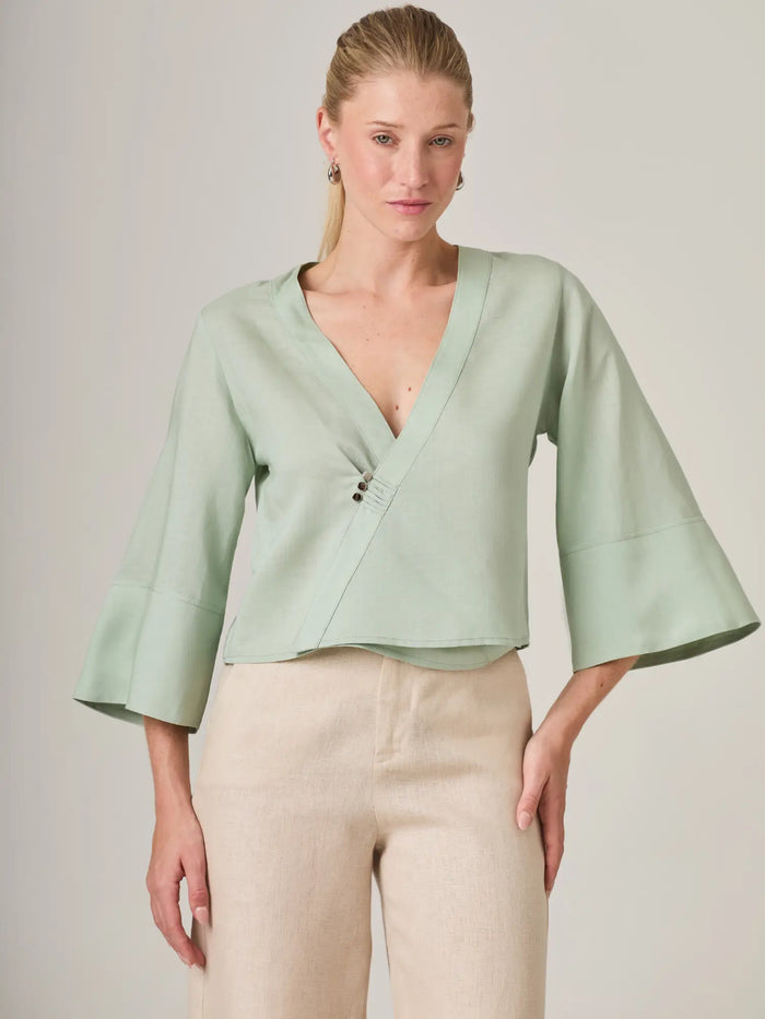 Blusa verde menta para mujer con elegante diseño cruzado y escote en V que estiliza la silueta. La blusa micaela es ideal para looks modernos y femeninos, perfecta para combinar con pantalones claros o faldas de lino.