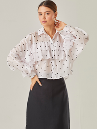 Esta blusa vaporosa de silueta relajada combina un estampado clásico de lunares con detalles delicados. Tiene cuello camisero, abotonadura frontal y volantes diagonales que recorren tanto el frente como las mangas, aportando movimiento y volumen. Su acabado semitransparente realza la ligereza de la prenda, perfecta para looks sofisticados con un toque divertido

Detalles:

Color: Ivory

Material: 100% Lyocel