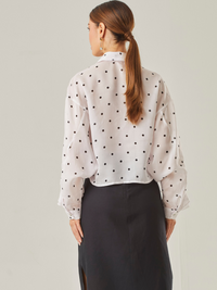 Esta blusa vaporosa de silueta relajada combina un estampado clásico de lunares con detalles delicados. Tiene cuello camisero, abotonadura frontal y volantes diagonales que recorren tanto el frente como las mangas, aportando movimiento y volumen. Su acabado semitransparente realza la ligereza de la prenda, perfecta para looks sofisticados con un toque divertido

Detalles:

Color: Ivory

Material: 100% Lyocel