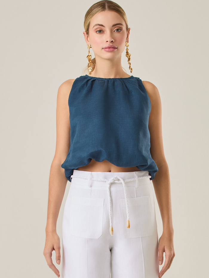Blusa de estilo relajado destaca por su escote redondeado y un sutil efecto de fruncido en el cuello, que aporta un toque delicado. Su corte fluido y sin mangas la convierte en una prenda fresca y versátil, perfecta para looks casuales o para combinar con piezas más estructuradas. Ideal para días cálidos, añadiendo comodidad sin perder elegancia