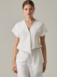 Blusa corta con silueta asimétrica y escote en V profundo. El diseño se cruza en el frente y se asegura con un botón al centro, generando una caída fluida y ligera. Las mangas cortas tipo capa aportan un aire moderno y relajado. Una prenda que combina líneas limpias con un toque contemporáneo.

Detalles:

Color: Blanco Perla

Material: 92% Rayón 8% Poliéster 