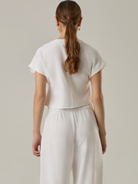 Blusa corta con silueta asimétrica y escote en V profundo. El diseño se cruza en el frente y se asegura con un botón al centro, generando una caída fluida y ligera. Las mangas cortas tipo capa aportan un aire moderno y relajado. Una prenda que combina líneas limpias con un toque contemporáneo.

Detalles:

Color: Blanco Perla

Material: 92% Rayón 8% Poliéster 
