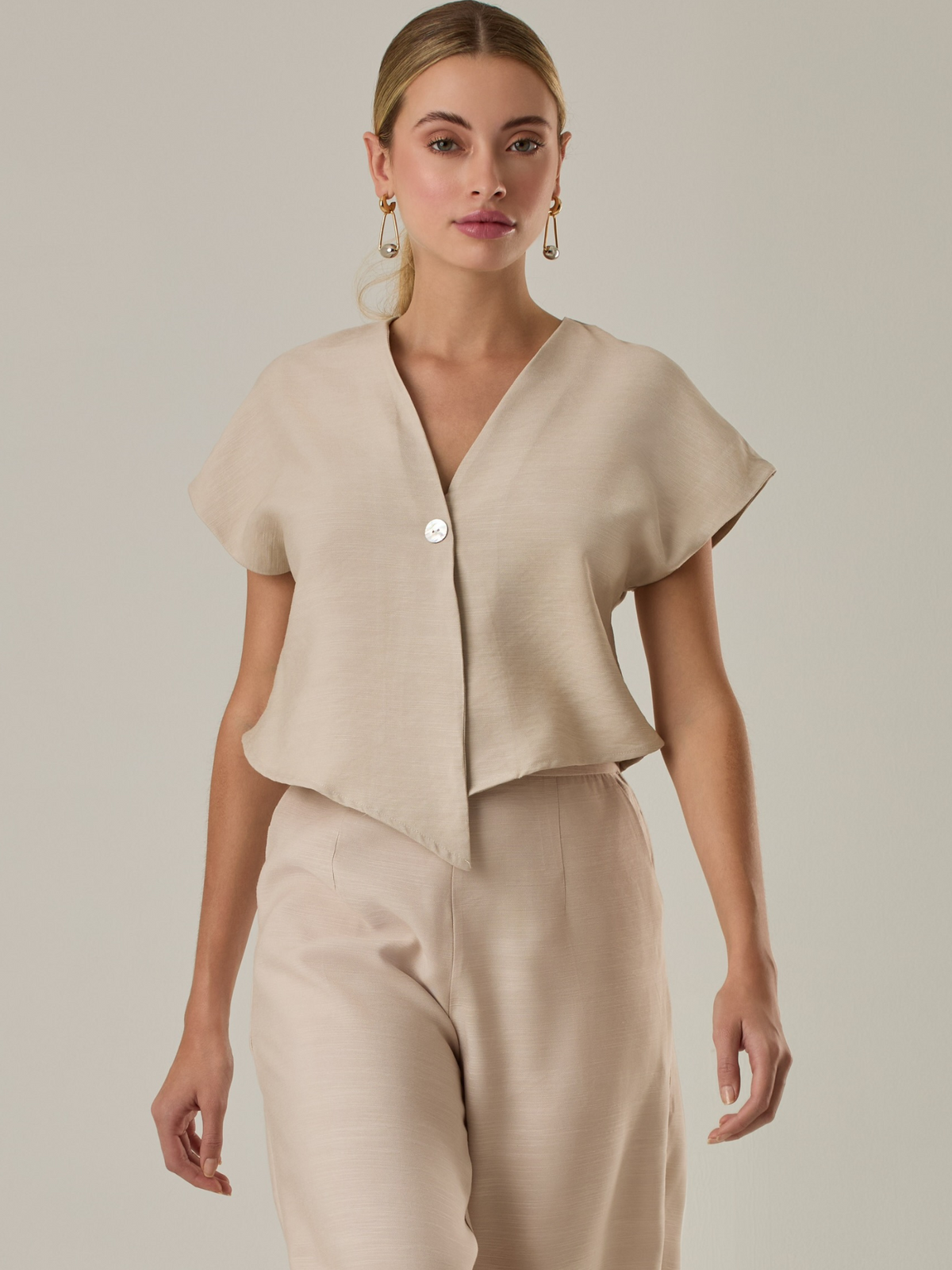 Blusa corta con silueta asimétrica y escote en V profundo. El diseño se cruza en el frente y se asegura con un botón al centro, generando una caída fluida y ligera. Las mangas cortas tipo capa aportan un aire moderno y relajado. Una prenda que combina líneas limpias con un toque contemporáneo.

Detalles:

Color: Sand

Material: 92% Rayón 8% Poliéster 