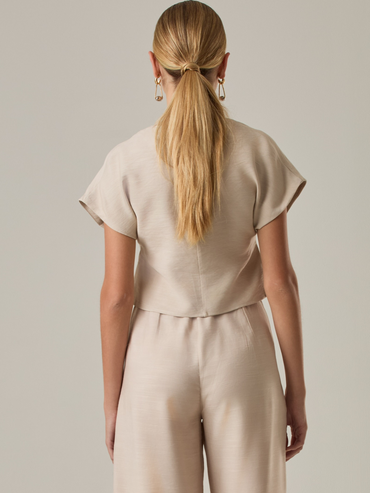 Blusa corta con silueta asimétrica y escote en V profundo. El diseño se cruza en el frente y se asegura con un botón al centro, generando una caída fluida y ligera. Las mangas cortas tipo capa aportan un aire moderno y relajado. Una prenda que combina líneas limpias con un toque contemporáneo.

Detalles:

Color: Sand

Material: 92% Rayón 8% Poliéster 