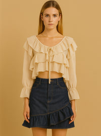 Fresca y femenina, esta blusa corta destaca por sus delicados volantes en el escote y el cuerpo, creando movimiento y suavidad visual. Con mangas largas de puño fruncido y amarre en el escote, es una prenda ideal para looks bohemios y estilismos relajados con un toque romántico. Perfecta para combinar con prendas de tiro alto en ocasiones casuales con estilo.