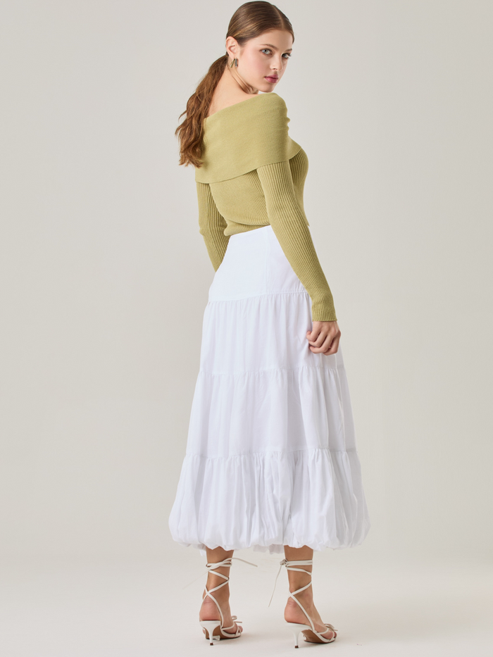 Esta es una falda blanca de largo midi con un diseño en capas que crea un efecto abombado en la parte inferior. Está hecha en una tela liviana y con caída. Tiene un estilo romántico y femenino, ideal para combinar con blusas ajustadas o crop tops. En la imagen se lleva con un suéter off-shoulder que le da un look sofisticado.