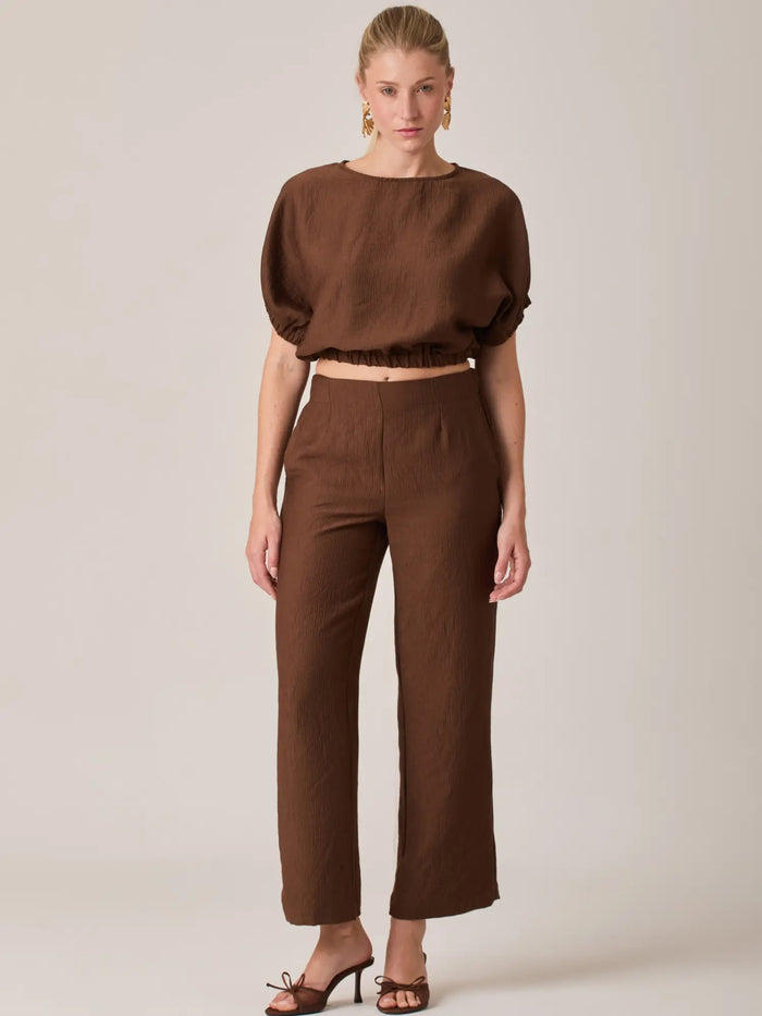 El Pantalón Largo Agostina Café presenta un diseño de tiro alto con caída recta que estiliza la figura. Ideal para looks elegantes o casuales, es una prenda versátil perfecta para el día a día.