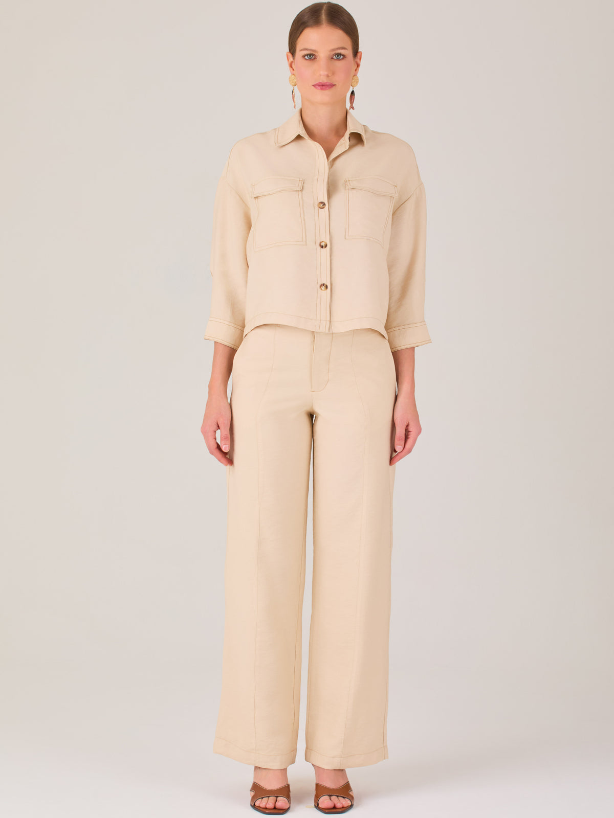 Este pantalón tiene un diseño sofisticado y moderno, confeccionado en un tono beige claro muy versátil. Presenta una silueta de pierna recta y ligeramente amplia, lo que aporta una caída elegante y cómoda. La cintura es de talle medio-alto, con cierre delantero oculto y detalles de pinzas que estilizan la figura. Incluye trabillas para cinturón y bolsillos laterales funcionales, además de costuras marcadas al frente que aportan estructura. Es una prenda ideal para looks de oficina, conjuntos monocromáticos 