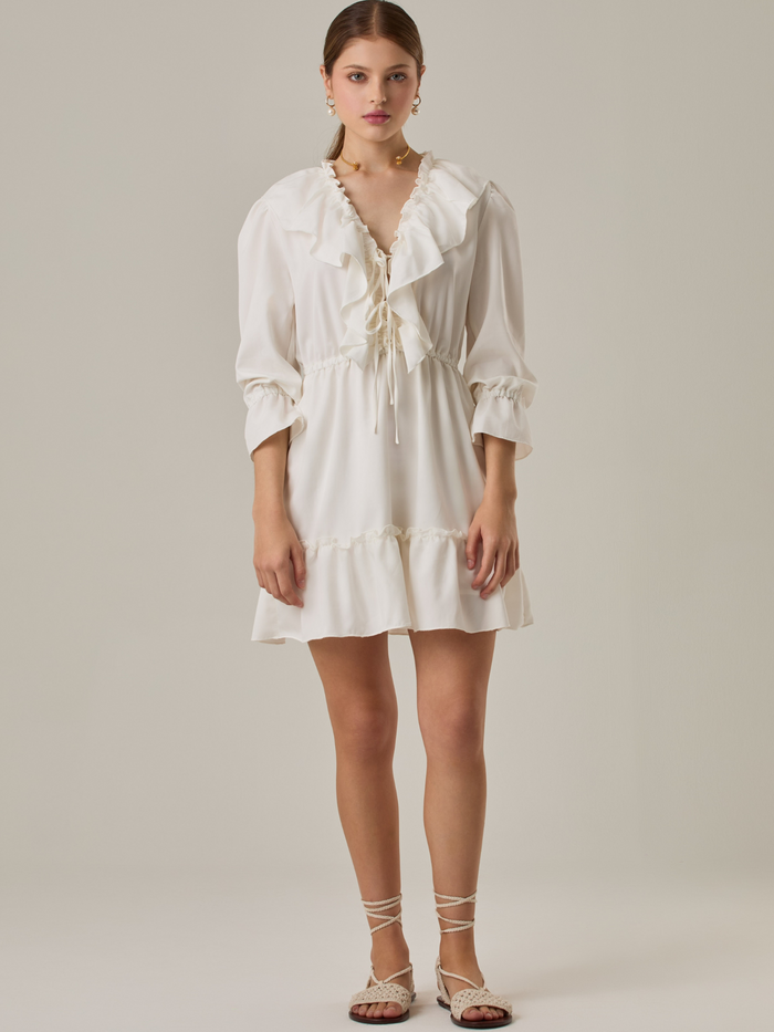 Vestido corto con volantes en el escote en V y en el ruedo. Tiene mangas largas con puños fruncidos y ajuste en la cintura con cordón. Su estilo femenino y romántico lo hace ideal para ocasiones casuales con un toque delicado.