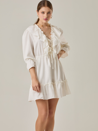 Vestido corto con volantes en el escote en V y en el ruedo. Tiene mangas largas con puños fruncidos y ajuste en la cintura con cordón. Su estilo femenino y romántico lo hace ideal para ocasiones casuales con un toque delicado.
