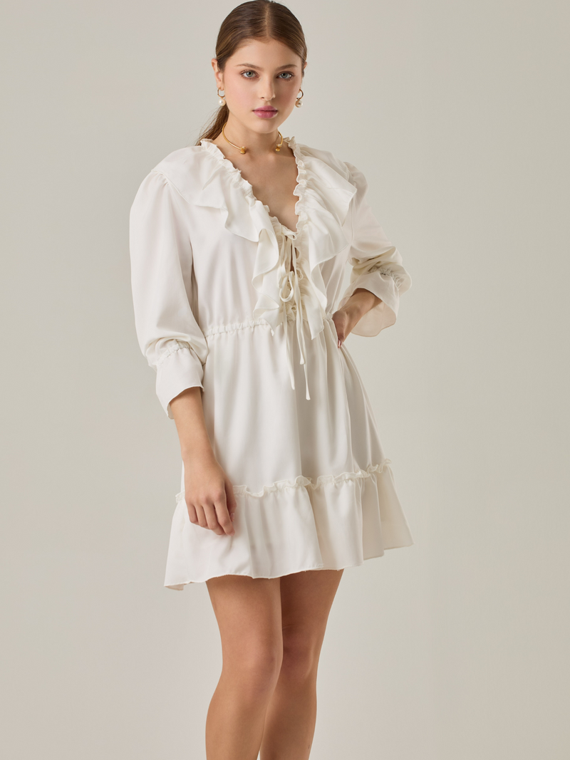 Vestido corto con volantes en el escote en V y en el ruedo. Tiene mangas largas con puños fruncidos y ajuste en la cintura con cordón. Su estilo femenino y romántico lo hace ideal para ocasiones casuales con un toque delicado.