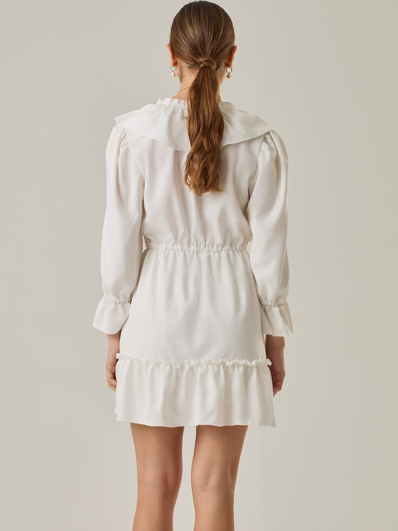Vestido corto con volantes en el escote en V y en el ruedo. Tiene mangas largas con puños fruncidos y ajuste en la cintura con cordón. Su estilo femenino y romántico lo hace ideal para ocasiones casuales con un toque delicado.

Detalles:

Color: Blanco Perla 