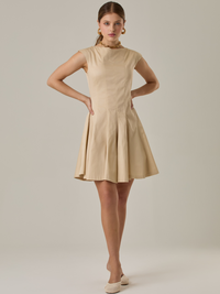 Vestido corto con silueta entallada en la parte superior y falda amplia. Tiene cuello cerrado tipo caja, mangas pequeñas que apenas cubren los hombros y costuras que definen la estructura del torso. La falda incorpora pliegues profundos que le dan volumen y movimiento. El largo llega por encima de la rodilla. Cierre invisible en la espalda.

Detalles:

Color: Ivory