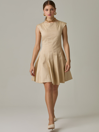 Vestido corto con silueta entallada en la parte superior y falda amplia. Tiene cuello cerrado tipo caja, mangas pequeñas que apenas cubren los hombros y costuras que definen la estructura del torso. La falda incorpora pliegues profundos que le dan volumen y movimiento. El largo llega por encima de la rodilla. Cierre invisible en la espalda.