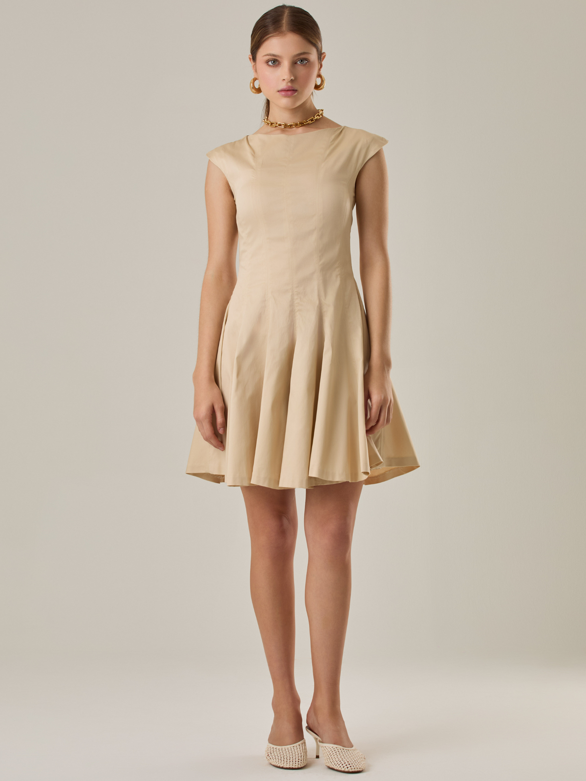 Vestido corto con silueta entallada en la parte superior y falda amplia. Tiene cuello cerrado tipo caja, mangas pequeñas que apenas cubren los hombros y costuras que definen la estructura del torso. La falda incorpora pliegues profundos que le dan volumen y movimiento. El largo llega por encima de la rodilla. Cierre invisible en la espalda.

Detalles:

Color: Ivory