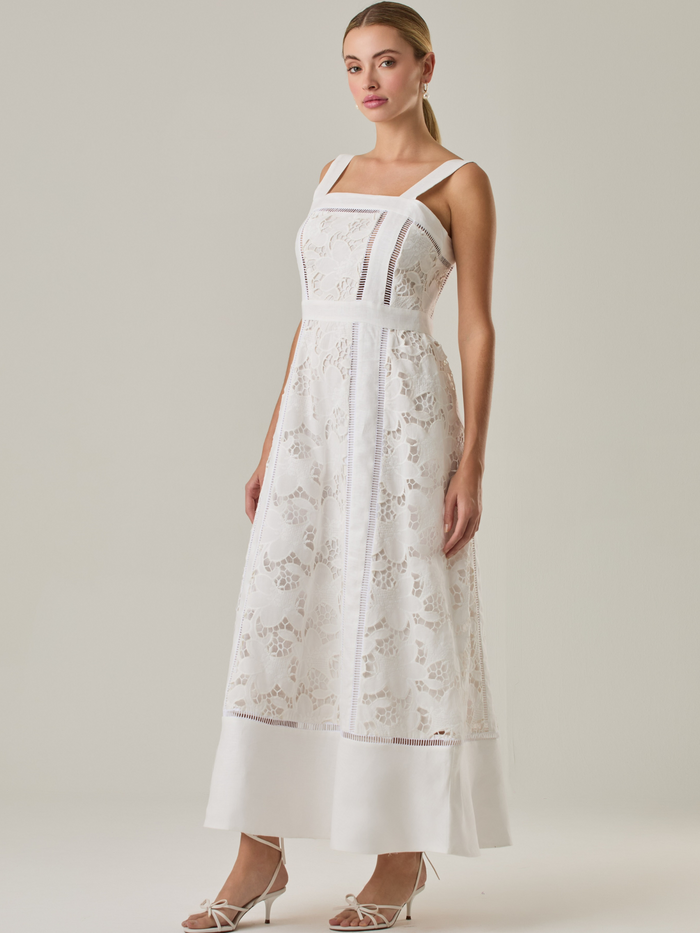 Vestido largo con tirantes anchos y escote recto, confeccionado en encaje floral con detalles calados que recorren el diseño de forma vertical. La base en contraste añade profundidad y estructura al diseño, mientras que el dobladillo liso aporta un toque de sobriedad que equilibra la delicadeza del encaje. Ideal para ocasiones especiales con un aire romántico y refinado.