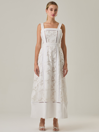 Vestido largo con tirantes anchos y escote recto, confeccionado en encaje floral con detalles calados que recorren el diseño de forma vertical. La base en contraste añade profundidad y estructura al diseño, mientras que el dobladillo liso aporta un toque de sobriedad que equilibra la delicadeza del encaje. Ideal para ocasiones especiales con un aire romántico y refinado.