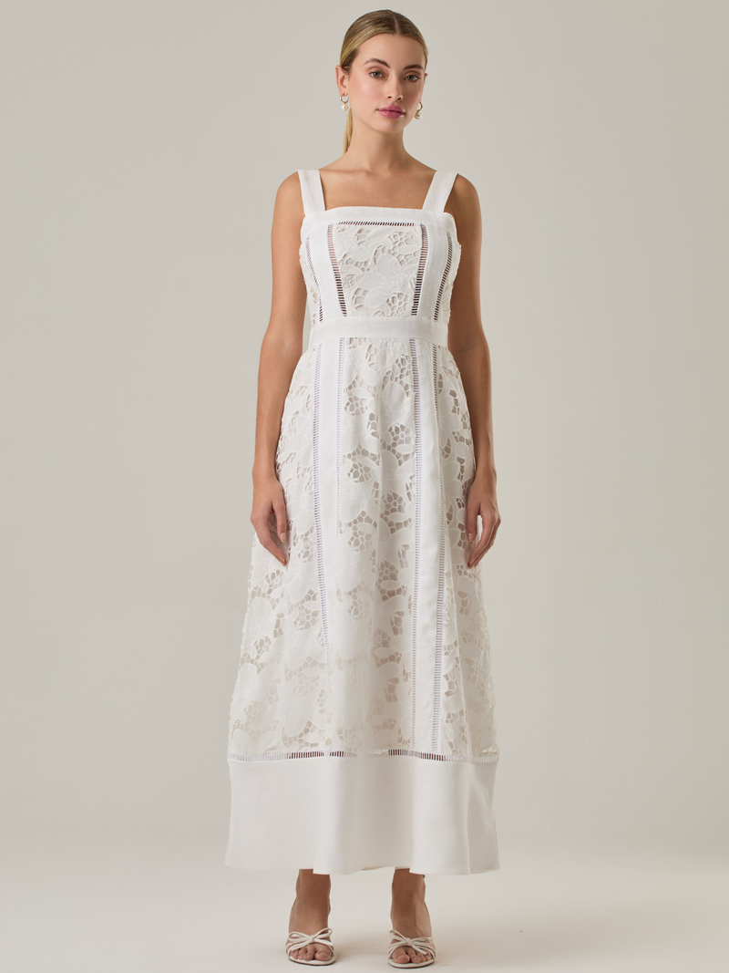 Vestido largo con tirantes anchos y escote recto, confeccionado en encaje floral con detalles calados que recorren el diseño de forma vertical. La base en contraste añade profundidad y estructura al diseño, mientras que el dobladillo liso aporta un toque de sobriedad que equilibra la delicadeza del encaje. Ideal para ocasiones especiales con un aire romántico y refinado.