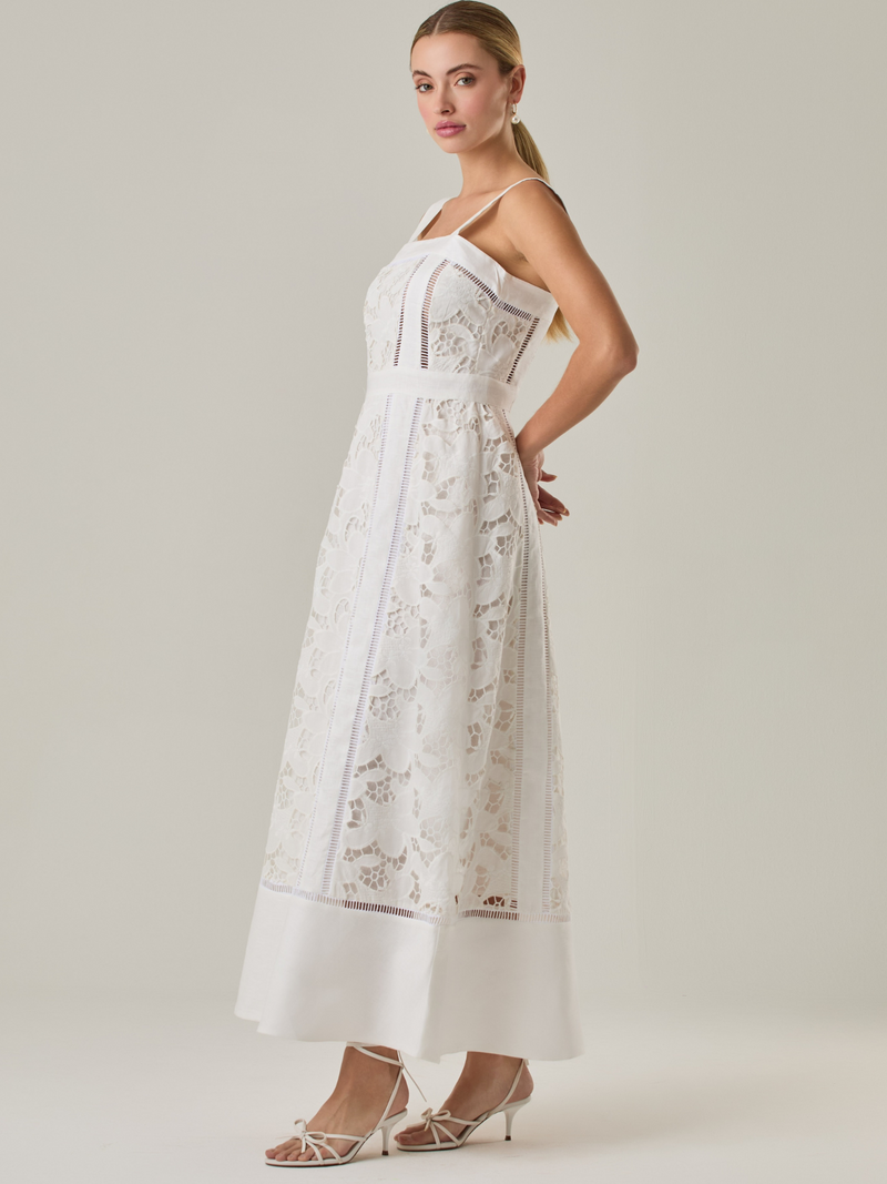 Vestido largo con tirantes anchos y escote recto, confeccionado en encaje floral con detalles calados que recorren el diseño de forma vertical. La base en contraste añade profundidad y estructura al diseño, mientras que el dobladillo liso aporta un toque de sobriedad que equilibra la delicadeza del encaje. Ideal para ocasiones especiales con un aire romántico y refinado.