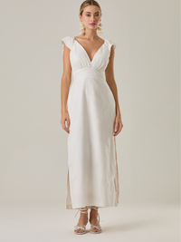 Este vestido tiene un aire delicado y femenino. Es de largo midi, con escote en “V” profundo al frente y en la espalda, y detalles de volantes en los tirantes. La parte trasera se ajusta con un lazo, dejando una abertura que resalta la cintura. El textil tiene un sutil bordado de hojas y flores, aportando textura sin ser recargado. El corte favorece la silueta y la abertura lateral en la falda añade movimiento al caminar. Ideal para eventos elegantes en climas cálidos.