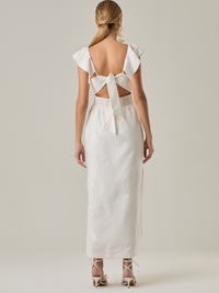 Este vestido tiene un aire delicado y femenino. Es de largo midi, con escote en “V” profundo al frente y en la espalda, y detalles de volantes en los tirantes. La parte trasera se ajusta con un lazo, dejando una abertura que resalta la cintura. El textil tiene un sutil bordado de hojas y flores, aportando textura sin ser recargado. El corte favorece la silueta y la abertura lateral en la falda añade movimiento al caminar. Ideal para eventos elegantes en climas cálidos.