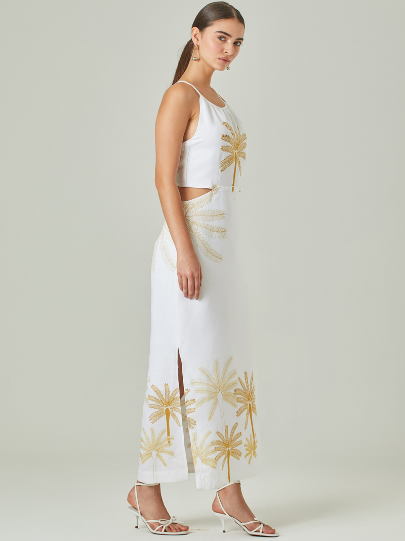 Vestido largo en color blanco con detalles dorados en forma de palmeras, ideal para un look sofisticado y veraniego. Su diseño con cuello halter y delicados cortes laterales realza la silueta con un toque moderno y elegante.