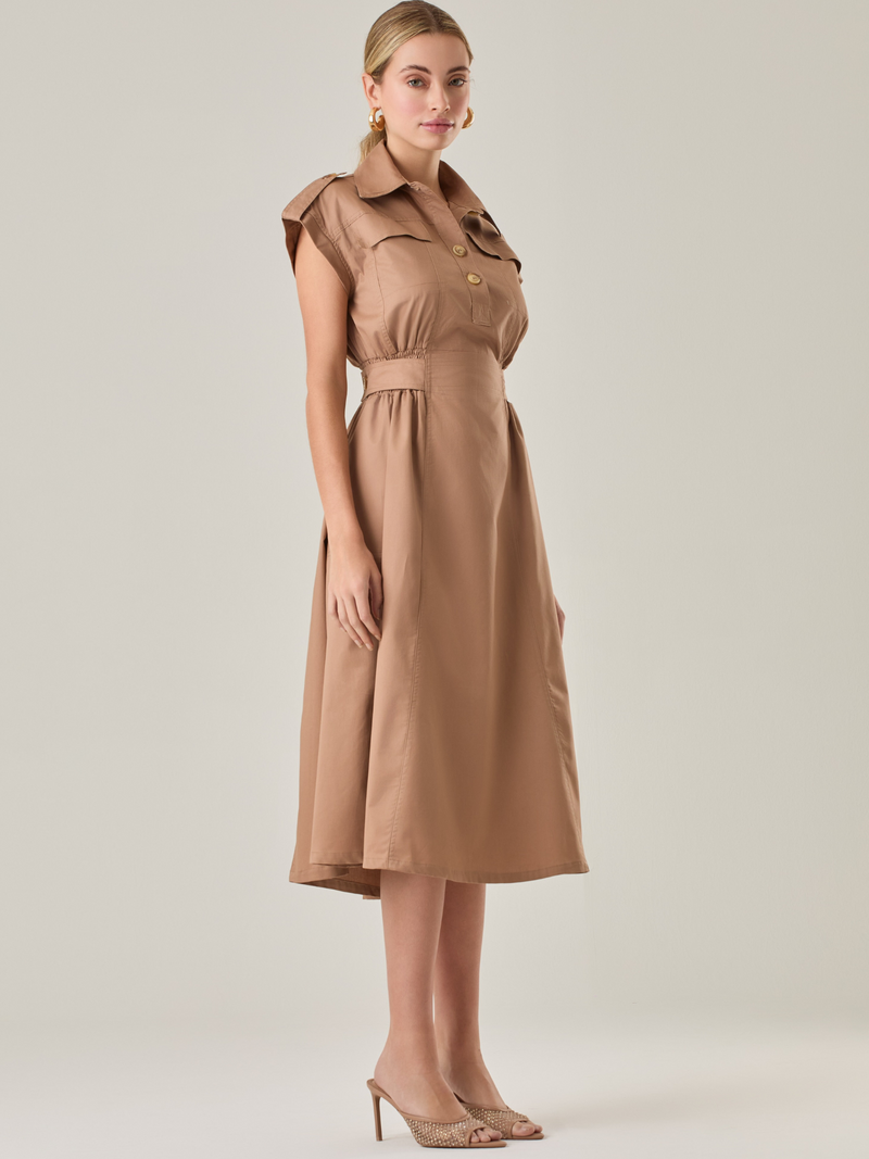 Vestido midi con inspiración safari, ideal para un look sofisticado y versátil. Su diseño con cuello camisero y botones aporta un aire elegante, mientras que los pliegues en la cintura estilizan la silueta. Los detalles en los hombros y los bolsillos decorativos añaden carácter a la prenda, combinando funcionalidad con estilo. Perfecto para combinar con sandalias o tacones y lograr un outfit atemporal.