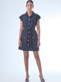 Vestido corto de estilo camisero con botones grandes al frente. Cuenta con cuello clásico, mangas cortas tipo casquillo y bolsillos de parche en el pecho y la parte baja del frente, que aportan un aire utilitario. La cintura se ajusta con un cinturón del mismo tejido, creando una silueta definida. Su diseño combina funcionalidad y sofisticación de manera equilibrada.

Detalles:

Color: Negro