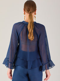 Ligera y romántica, esta blusa de textura vaporosa destaca por sus volantes en capas que aportan movimiento y fluidez. El escote en V y las mangas amplias con acabado ondulado añaden un toque delicado y sofisticado. Ideal para ocasiones especiales, cenas o estilismos casuales con un aire femenino y refinado.
