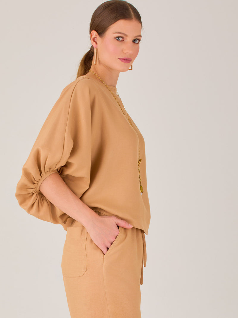 Con un diseño sobrio y sofisticado, esta blusa se distingue por su silueta recta y mangas globo tres cuartos con puño ajustado. El escote recto y el tejido con cuerpo le dan un aire minimalista ideal para combinar con pantalones de sastre o faldas estructuradas. Perfecta para elevar looks formales o casuales con discreta elegancia.