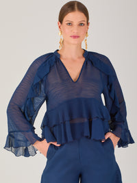 Ligera y romántica, esta blusa de textura vaporosa destaca por sus volantes en capas que aportan movimiento y fluidez. El escote en V y las mangas amplias con acabado ondulado añaden un toque delicado y sofisticado. Ideal para ocasiones especiales, cenas o estilismos casuales con un aire femenino y refinado.