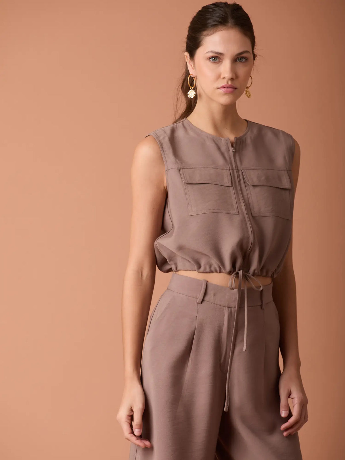 Blusa Ardaza Café corta con bolsillos superiores y cordón ajustable para un estilo casual sofisticado.