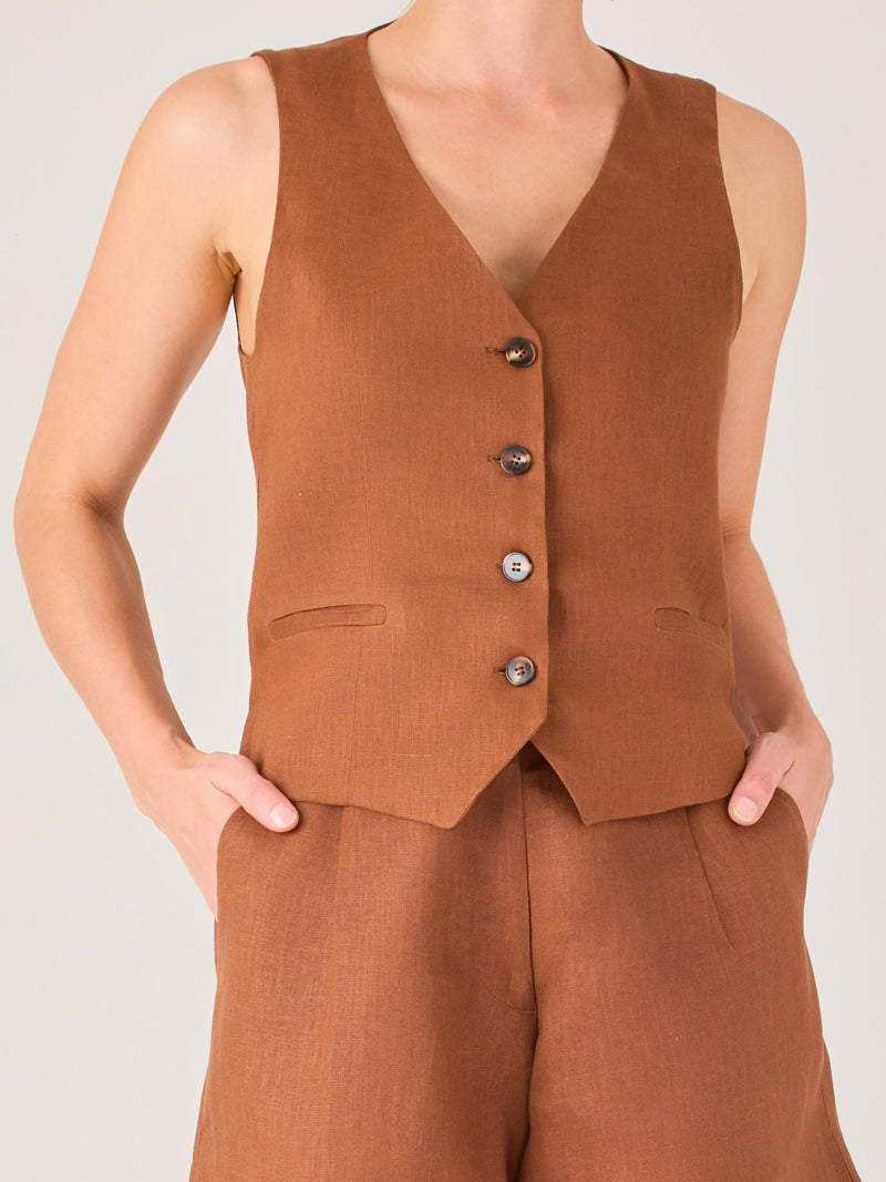 Esta blusa tipo chaleco es ideal para climas cálidos o para crear looks sofisticados con un aire casual. Presenta un corte recto ligeramente entallado que acentúa la silueta de forma sutil, y un escote en “V” que estiliza el cuello. Cuenta con una botonadura frontal compuesta por cinco botones oscuros que contrastan elegantemente con el tono neutro de la prenda. También incorpora bolsillos falsos decorativos a ambos lados del frente, que añaden un detalle sutil al diseño minimalista. Esta pieza es versátil 