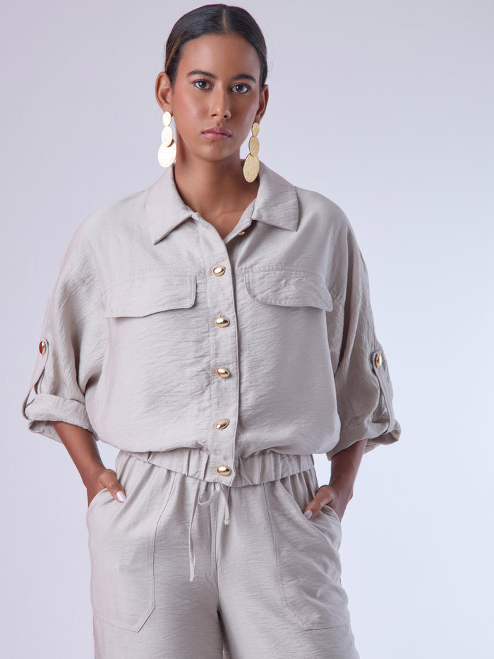 Relajada pero estructurada, esta blusa de silueta amplia combina un diseño utilitario con detalles refinados. Presenta bolsillos de solapa en el pecho, mangas con opción de ajuste y una botonadura dorada que aporta un toque de brillo sutil. Ideal para estilismos casuales con elegancia natural, o para elevar conjuntos relajados con una prenda clave y atemporal.