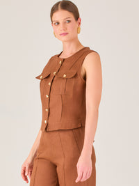 Esta elegante blusa sin mangas presenta un diseño estructurado tipo chaleco, confeccionada en un tejido de textura firme que aporta un aire sofisticado. El tono marrón chocolate refuerza su estilo clásico y versátil. Cuenta con un escote redondo cerrado y una botonadura central con botones metálicos de acabado dorado que destacan sobre el fondo oscuro.