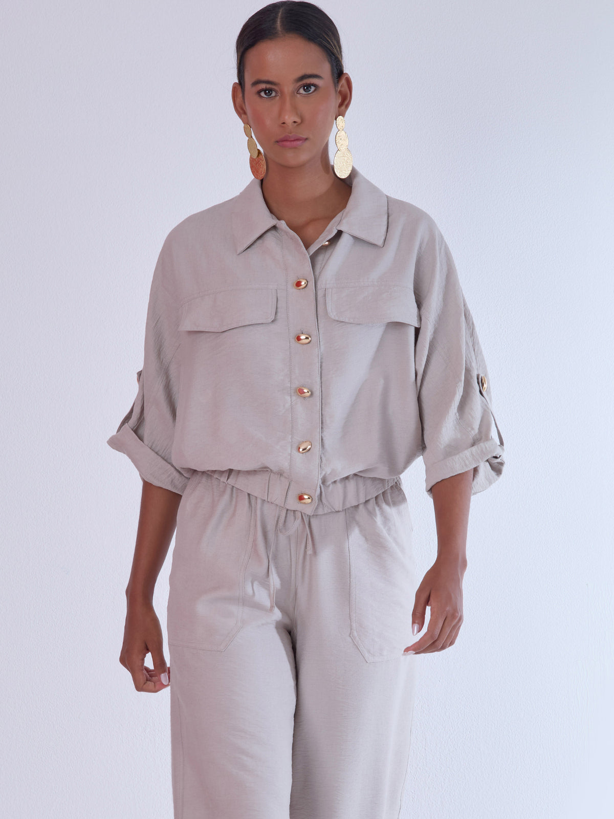 Relajada pero estructurada, esta blusa de silueta amplia combina un diseño utilitario con detalles refinados. Presenta bolsillos de solapa en el pecho, mangas con opción de ajuste y una botonadura dorada que aporta un toque de brillo sutil. Ideal para estilismos casuales con elegancia natural, o para elevar conjuntos relajados con una prenda clave y atemporal.
